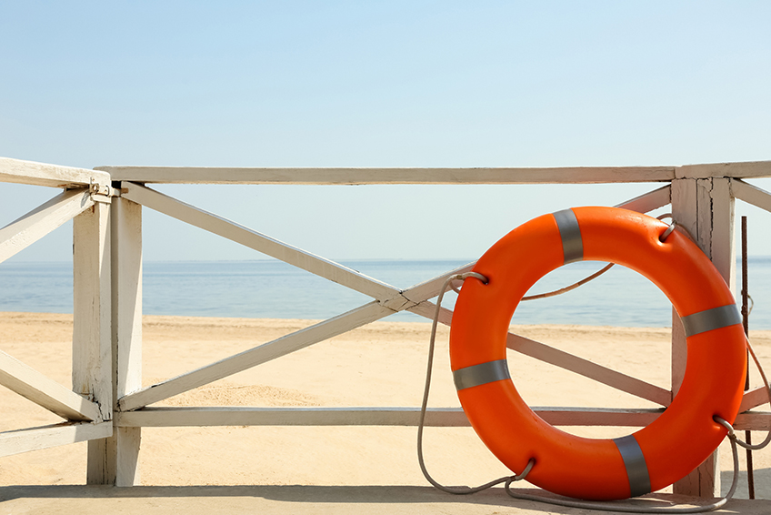 Image d'une bouée rouge contre un garde-corps donnant sur une plage