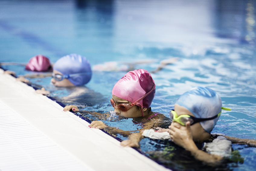Image de quatre enfants avec des bonnets de bain et lunettes de plongée au bord d'une piscine