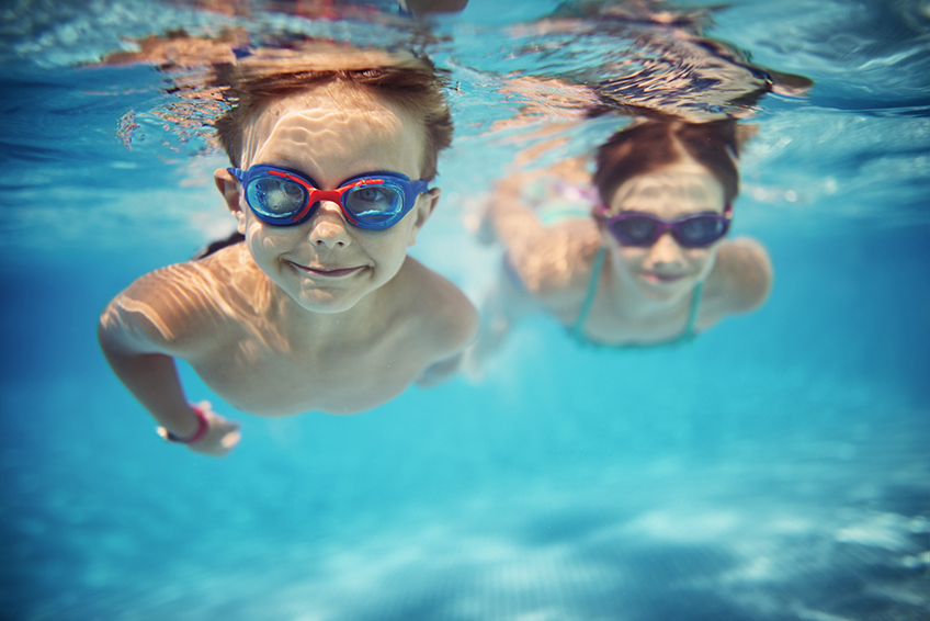Image avec deux enfants portant des lunettes de natation et nageant sous l'eau dans une piscine
