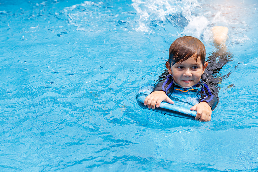 Image d'un petit garçon apprenant à nager dans une piscine avec une planche