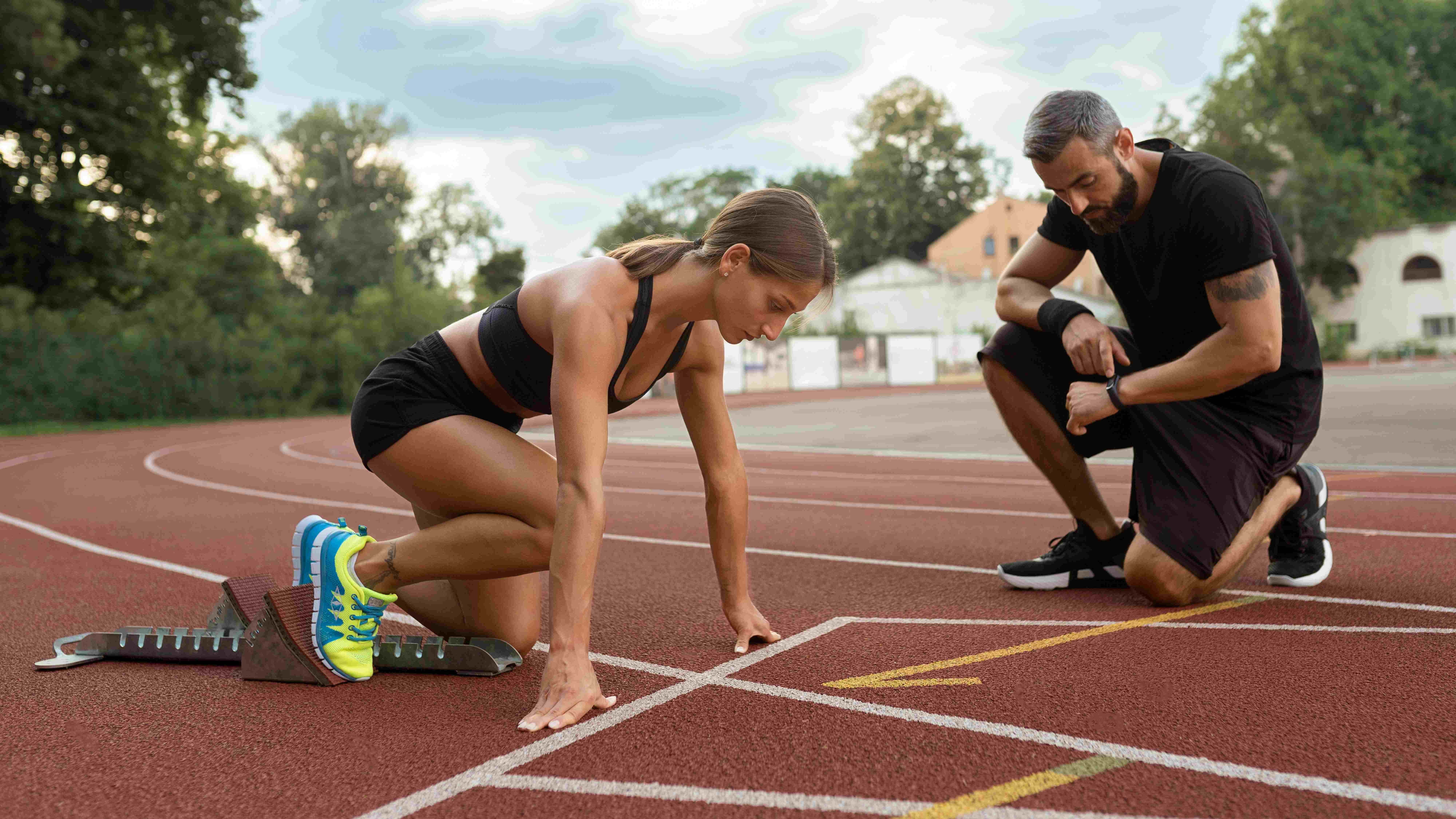 Femme sportive à la ligne de départ d'un stade d'athlétisme avec son coach en train de chronométrer