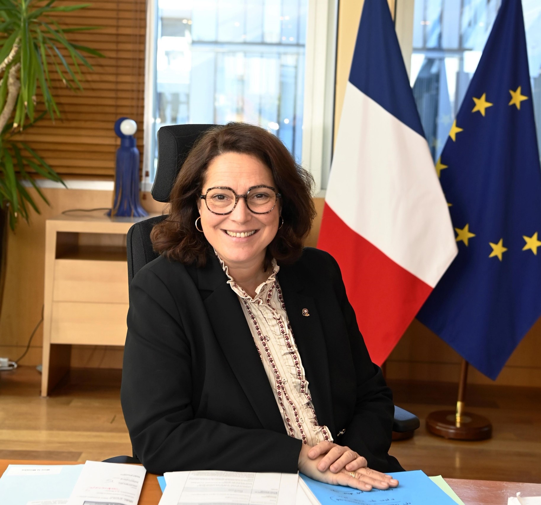 Photo officielle de Marina Ferrari assise à son bureau avec les drapeaux à l'arrière-plan
