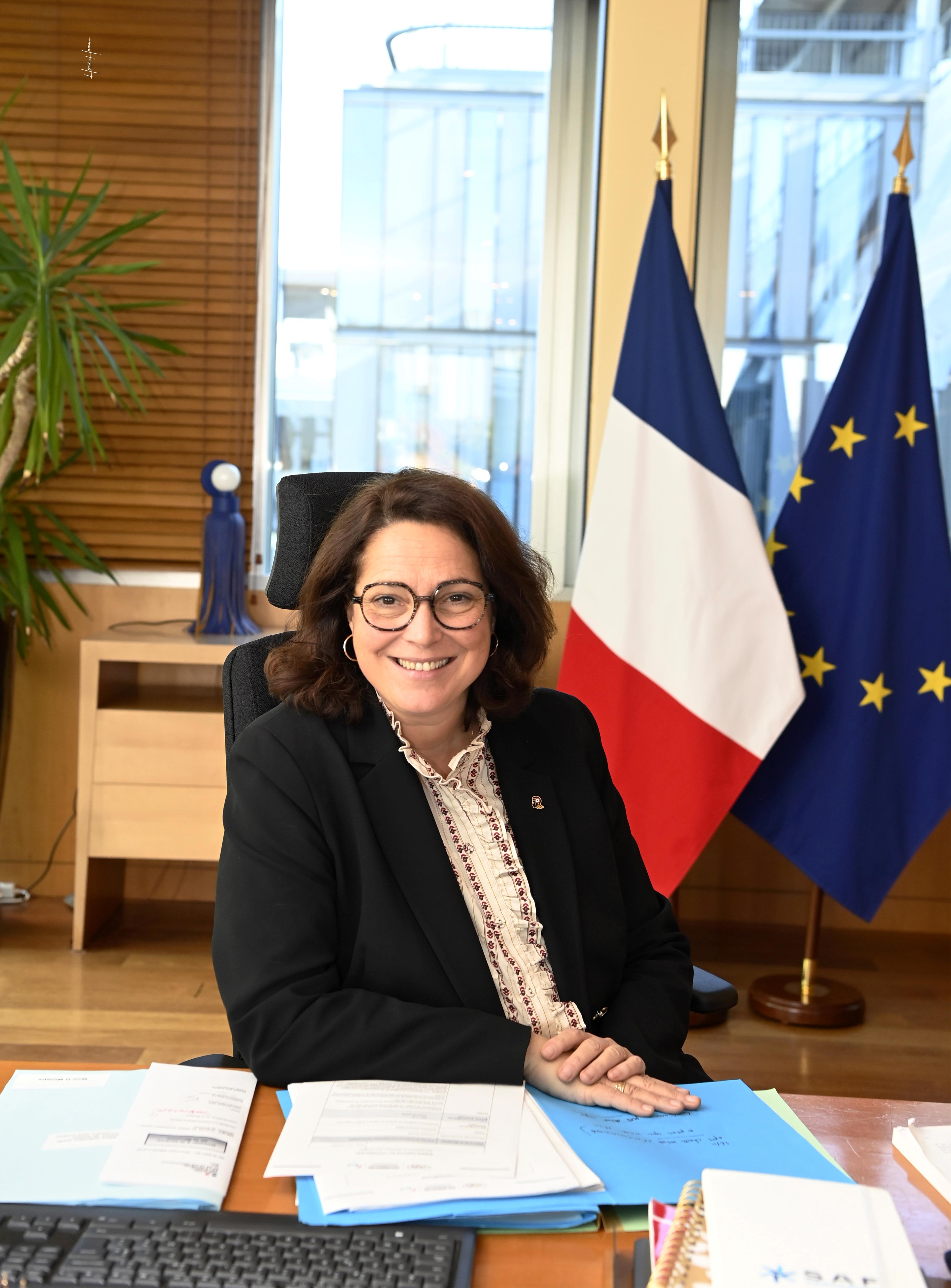 Photo officielle de Marina Ferrari assise à son bureau avec les drapeaux à l'arrière-plan