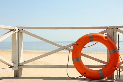 Image d'une bouée rouge contre un garde-corps donnant sur une plage