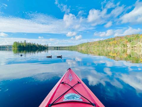 Photo d'un canoë sur un étang reflétant le bleu du ciel et les nuages