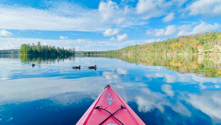 Photo d'un canoë sur un étang reflétant le bleu du ciel et les nuages