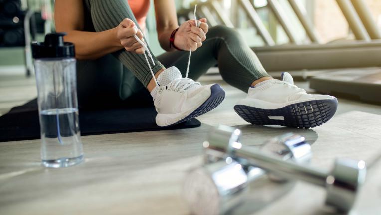 femme-athletique-attachant-une-chaussure-de-sport-au-club-de-sante