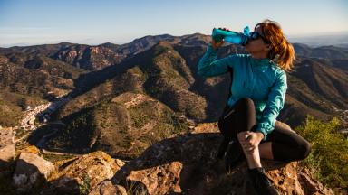 Femme qui boit dans sa gourde au sommet d'une montagne