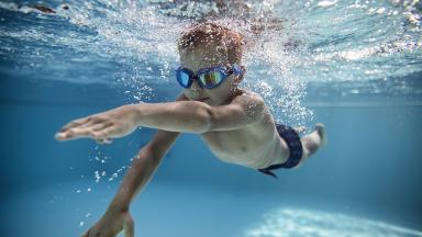 Image d'un enfant garçon avec des lunettes de natation en train de nager dans une piscine