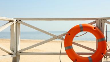 Image d'une bouée rouge contre un garde-corps donnant sur une plage