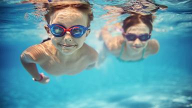Image avec deux enfants portant des lunettes de natation et nageant sous l'eau dans une piscine