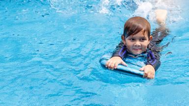 Image d'un petit garçon apprenant à nager dans une piscine avec une planche