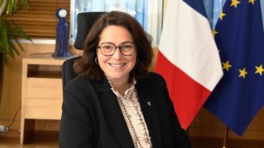Photo officielle de Marina Ferrari assise à son bureau avec les drapeaux à l'arrière-plan